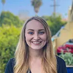 Anna G., Vice President of Operations, smiling on a sunny balcony with greenery and a blue sky in the background.