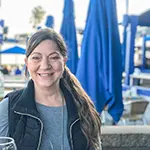 Gina G., Founder and CEO, smiling at an outdoor café with blue umbrellas in the background.